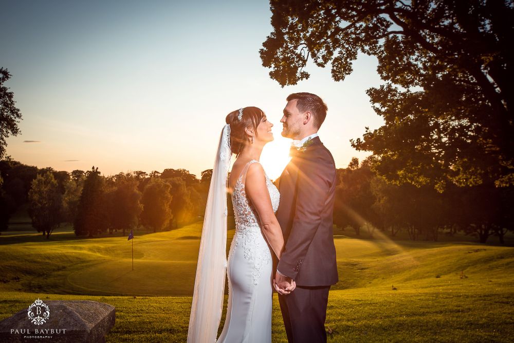 Golden sunset light illuminates couple on rolling golf course landscape.
