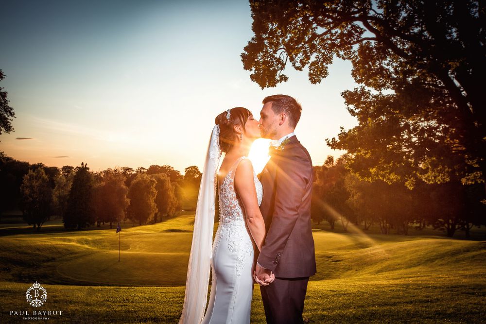 A romantic sunset wedding photo on a golf course with golden light streaming through trees.