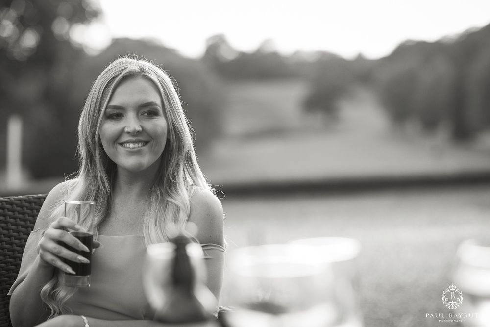 Black and white portrait of someone holding a drink glass at an outdoor event.