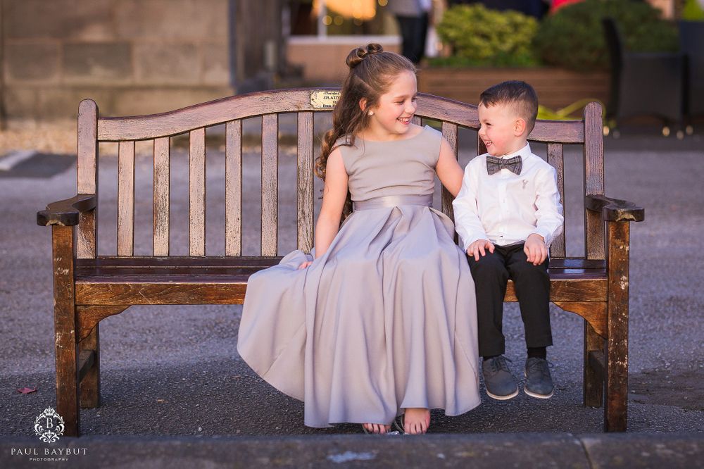 Two attendees in formal wear sitting together on a wooden bench at an event.