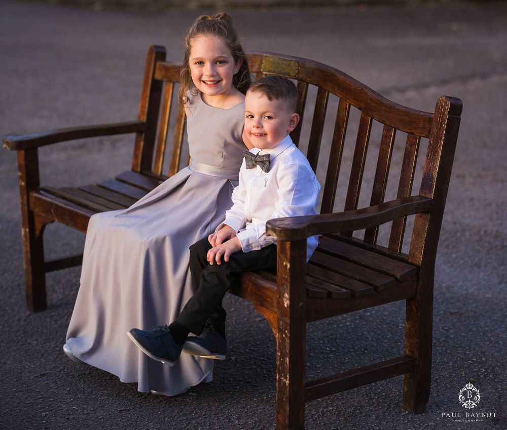 Color photo of two young attendees in formal wear sharing a bench at an event.