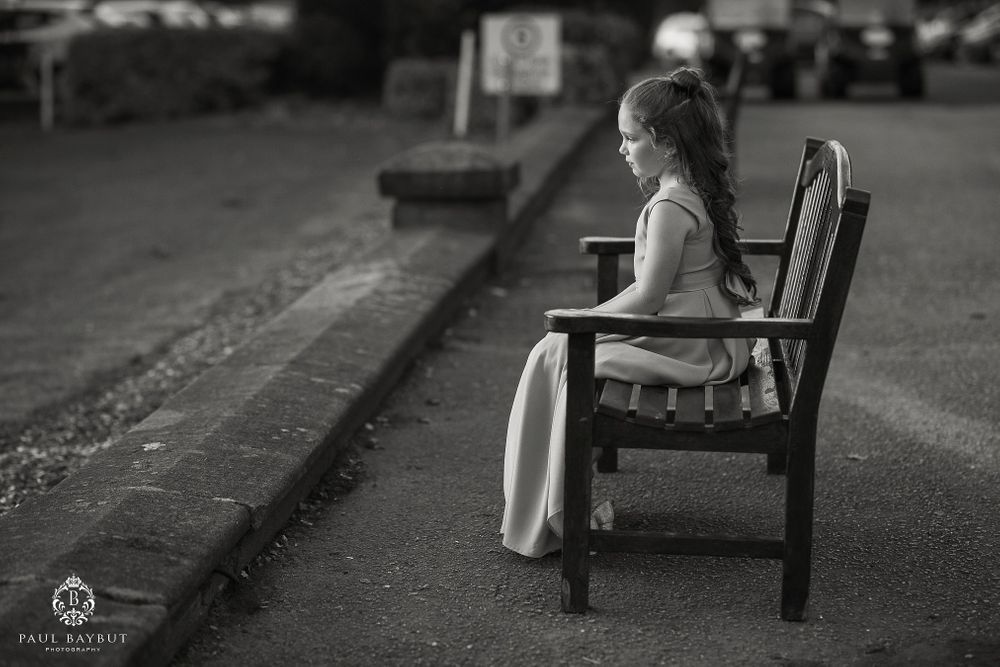 Black and white image of someone sitting alone on a bench in formal attire.