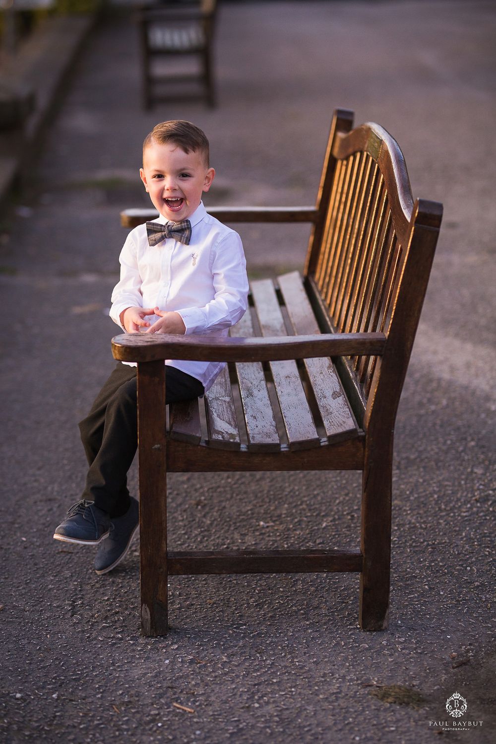 Young attendee in formal wear sitting on wooden bench outdoors.