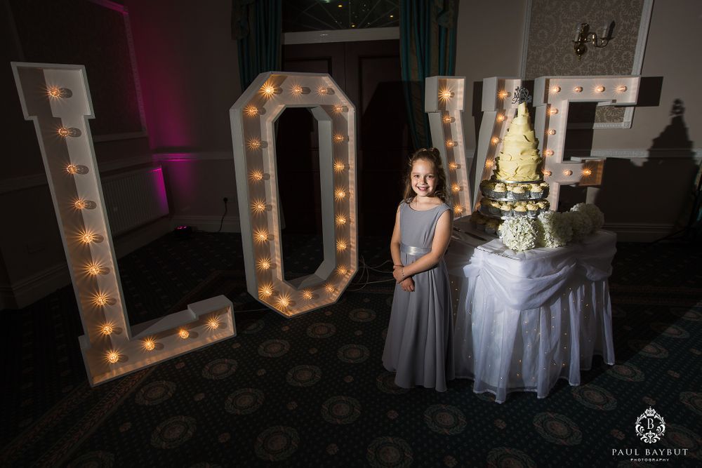 Large illuminated LOVE letters display with cake table at wedding reception.