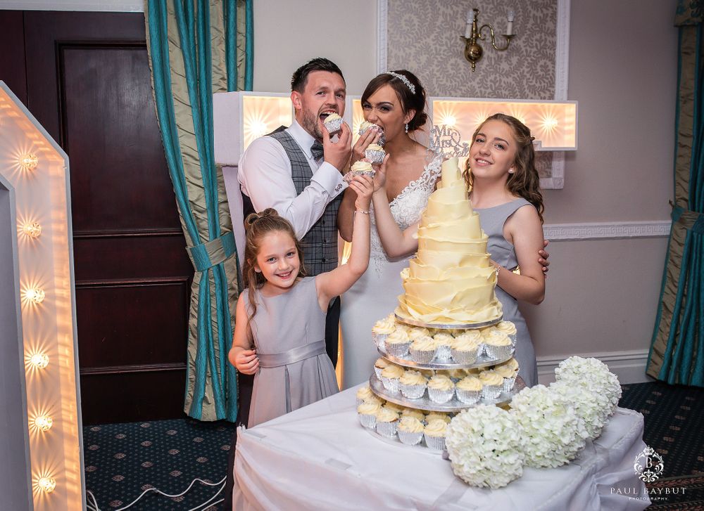 Wedding party gathered around a multi-tiered yellow cake during reception celebration.
