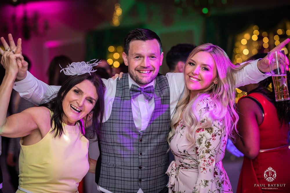 Wedding guests celebrating and posing together under vibrant pink lighting at reception party.