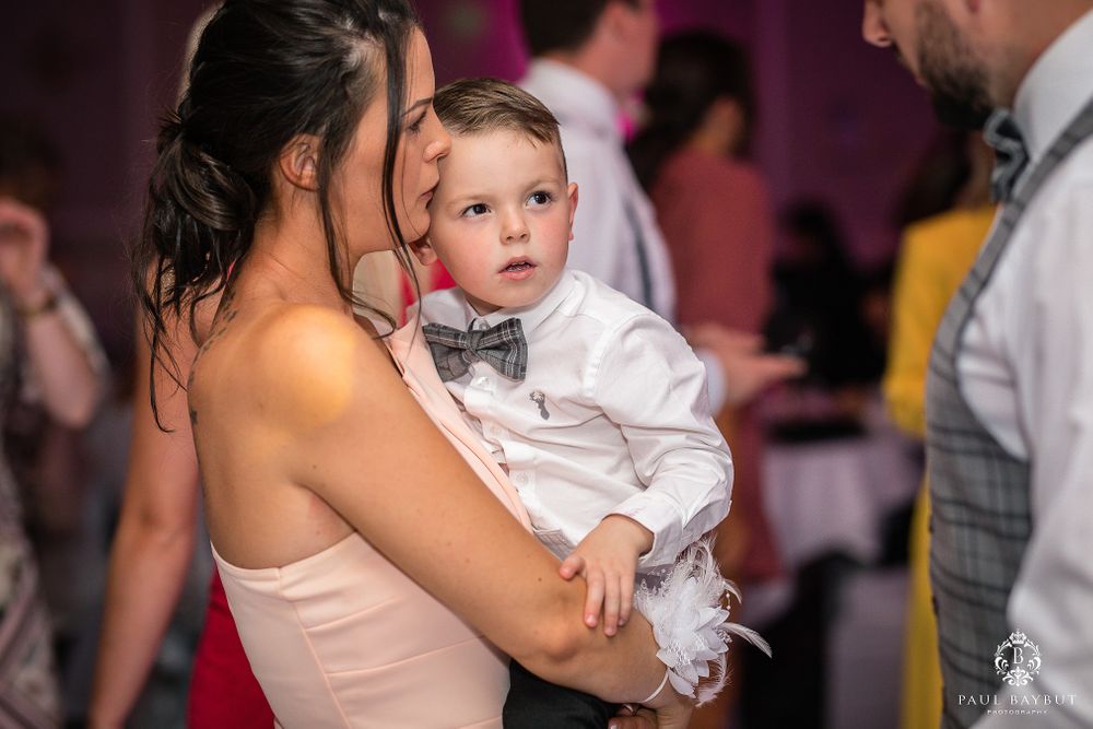 Guest in formal attire holding young boy in bow tie during wedding reception.
