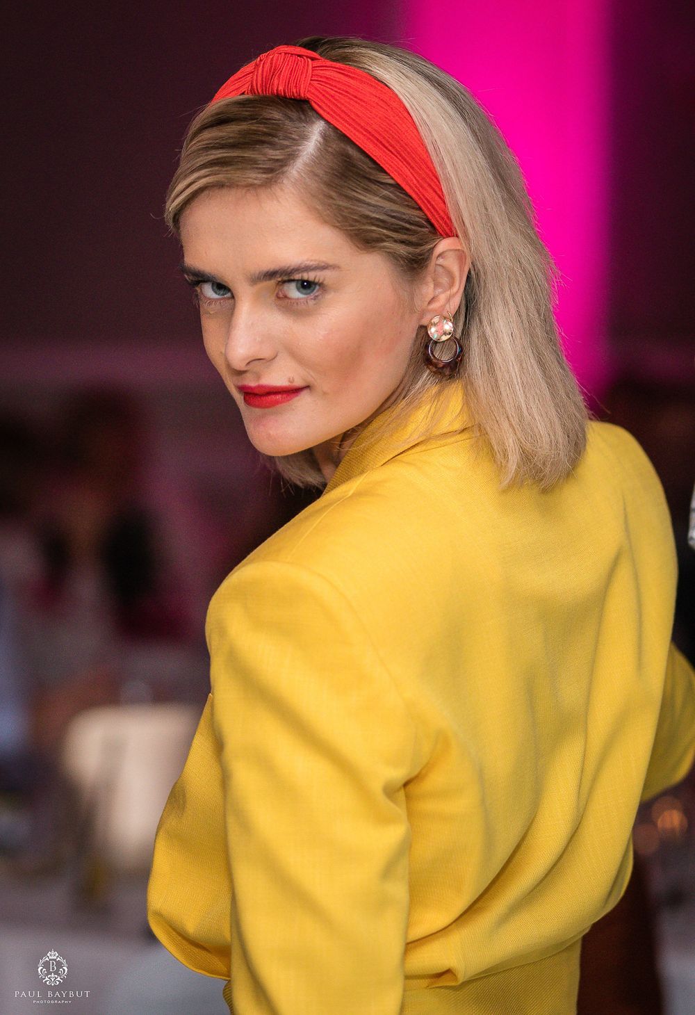 Stylish guest in yellow jacket and red headband at formal evening event.