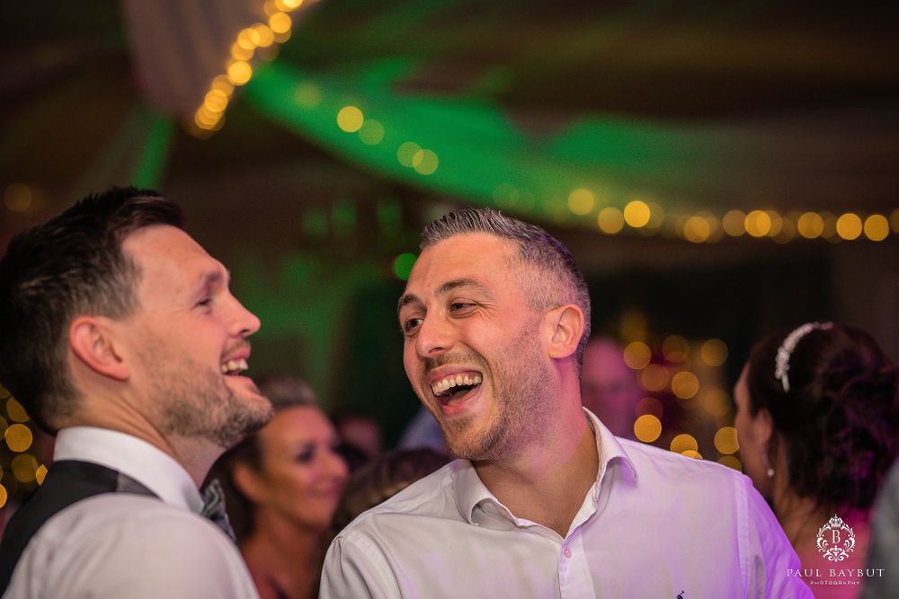Two guests share a laugh during an evening wedding celebration with colorful ambient lighting.