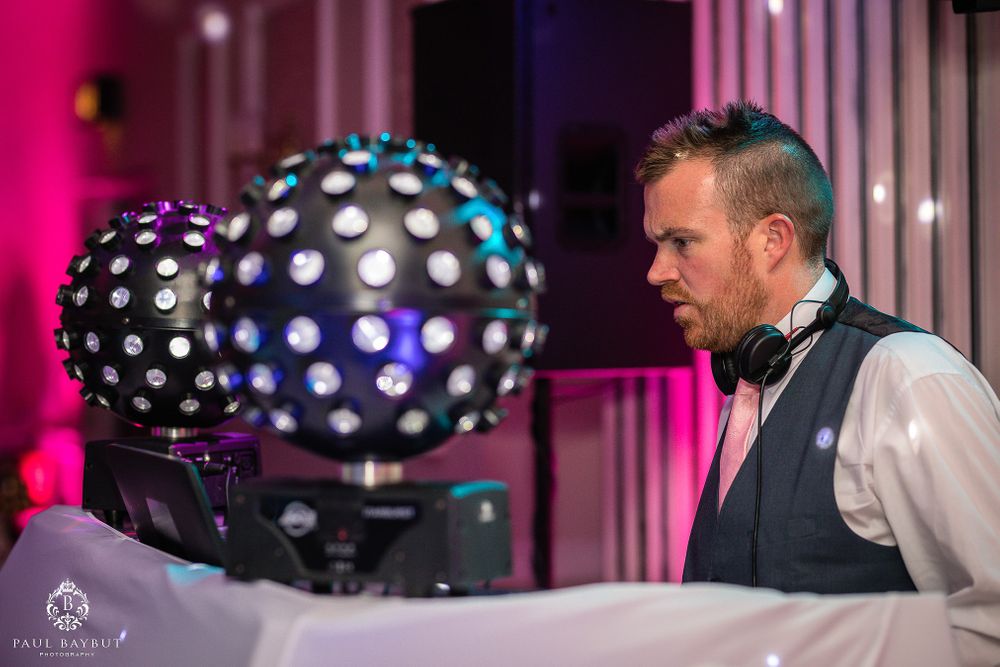 DJ performing at a wedding reception with illuminated disco balls and pink lighting effects.