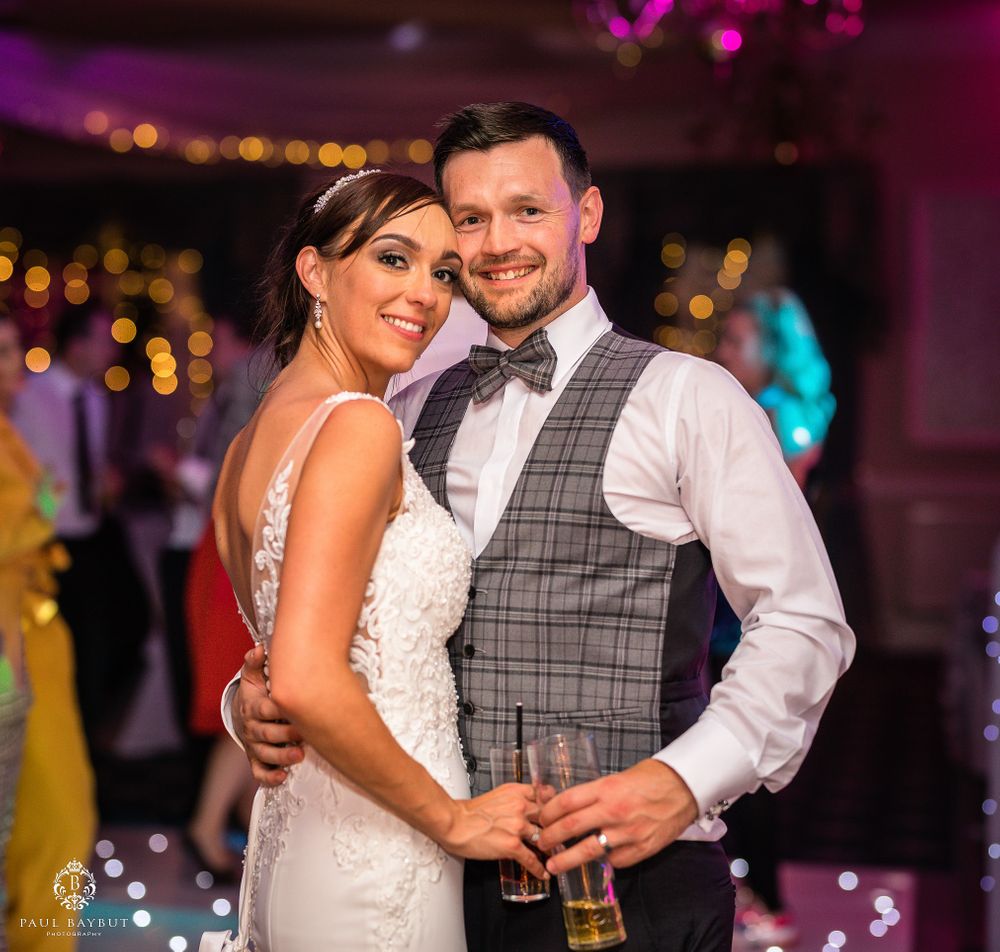 A couple embrace on their wedding day during their reception with festive lighting and decorations.