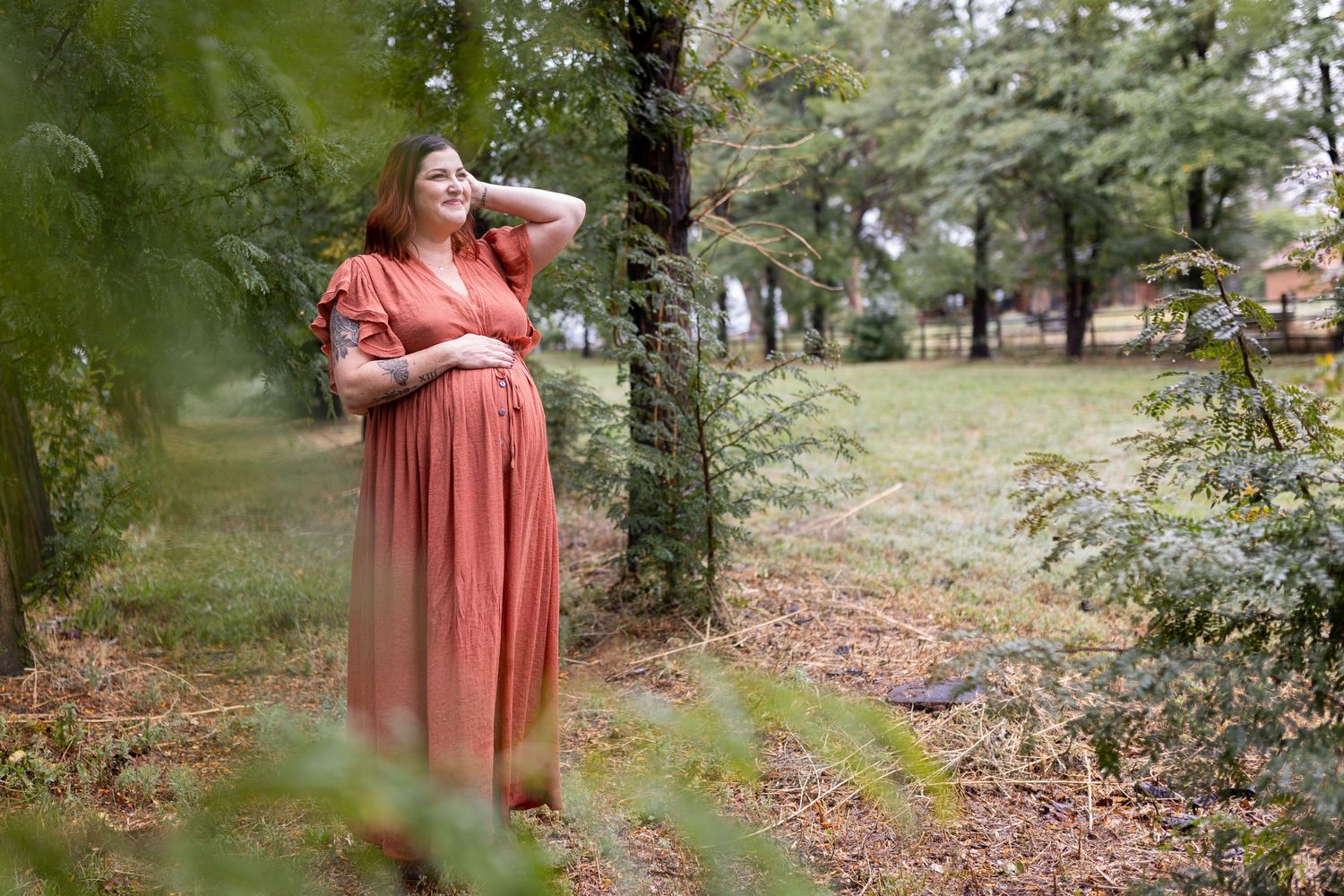 Woman with hand on pregnant stomach looking through the trees to the light during her maternity session