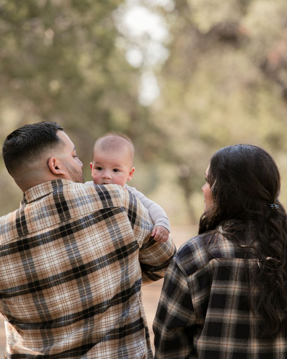 Family in plaid shirts sharing a tender moment outdoors in natural lighting.