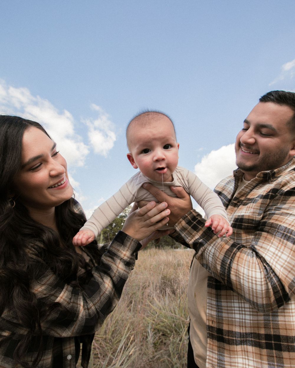 A playful family photoshoot in a field with natural lighting and plaid clothing.