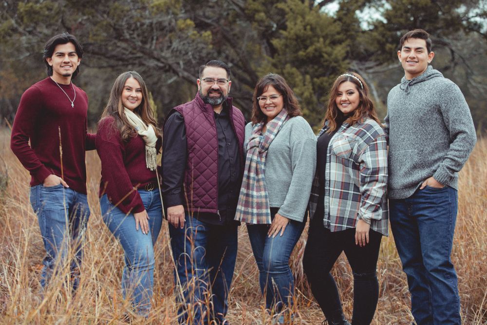 Large family group poses together in casual attire against a rustic outdoor backdrop.