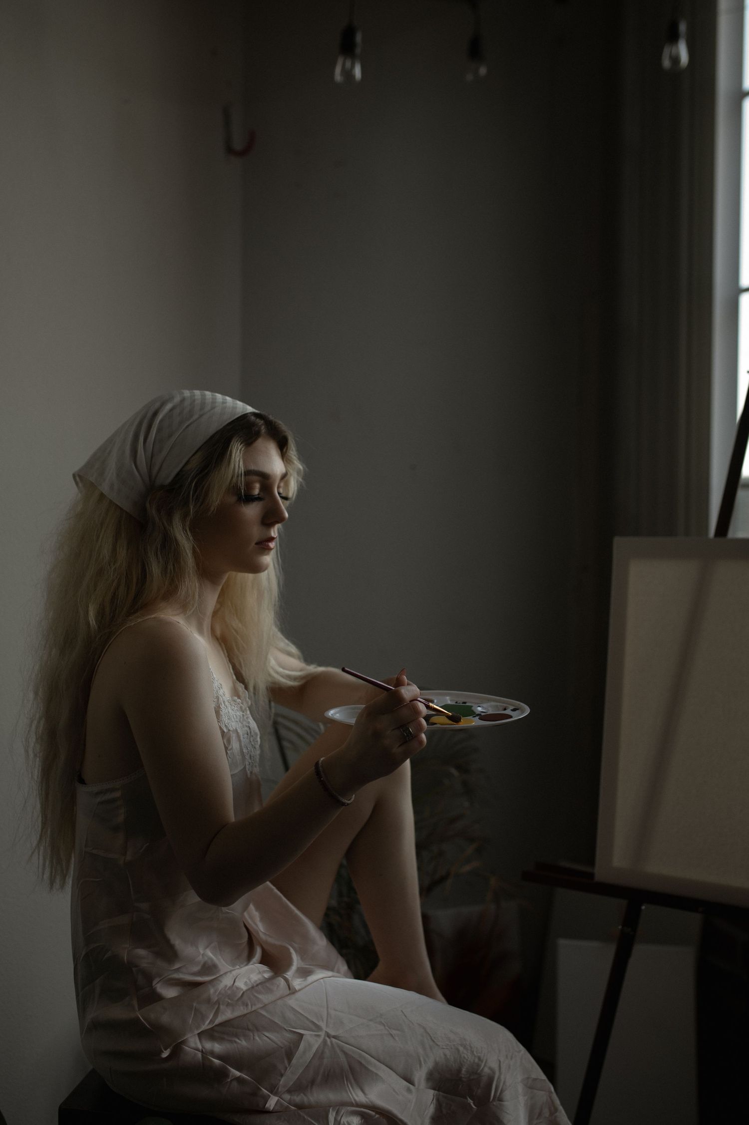 An artistic portrait of someone painting at an easel in soft, moody lighting.