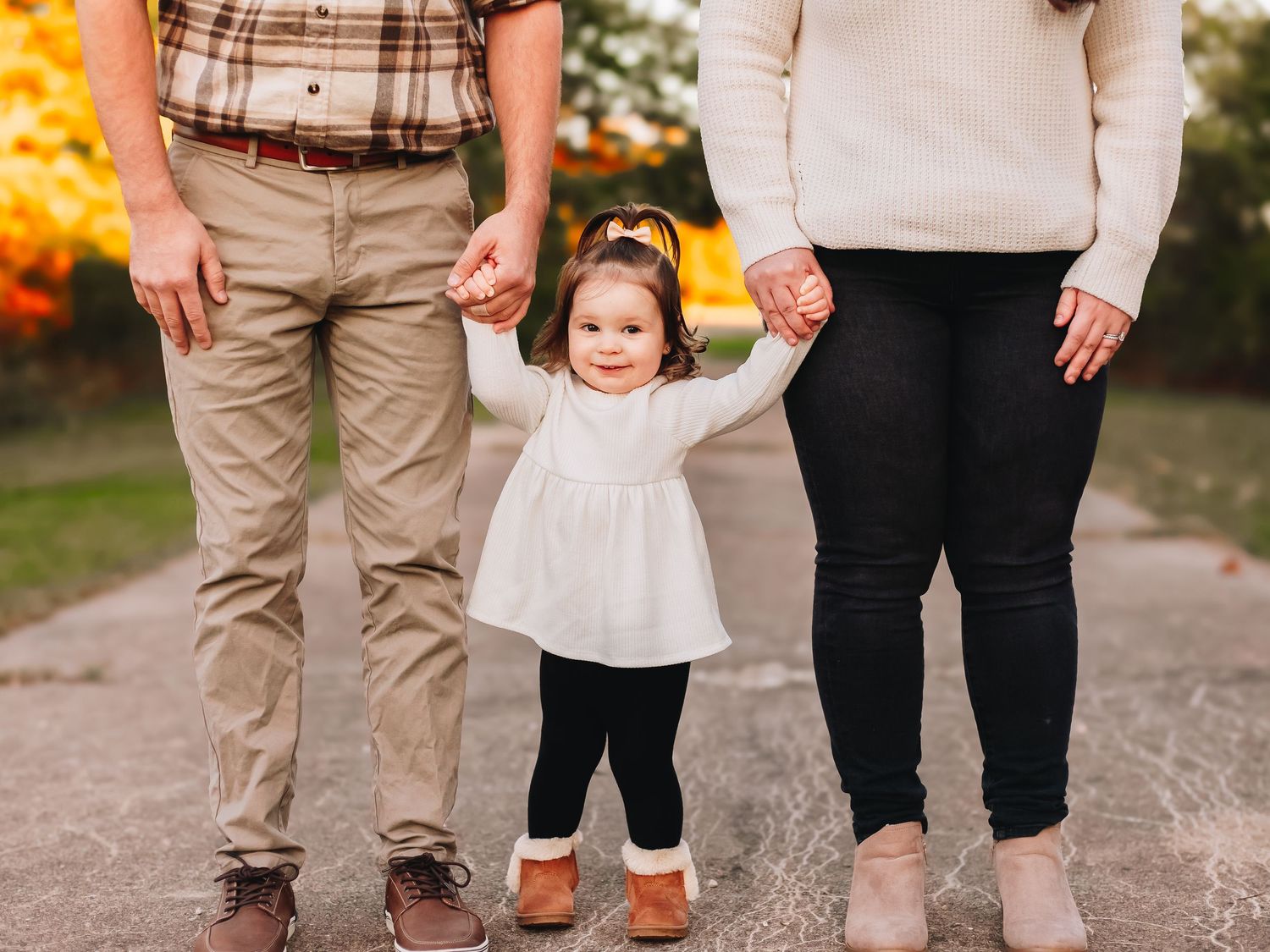 Candid lower body shot of family members wearing coordinated neutral fall outfits outdoors.