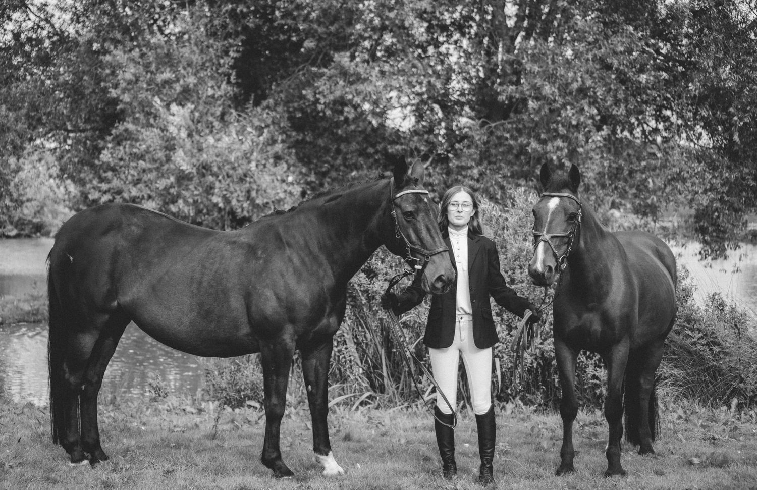Black and white photograph of two horses with their handler in a natural outdoor setting.