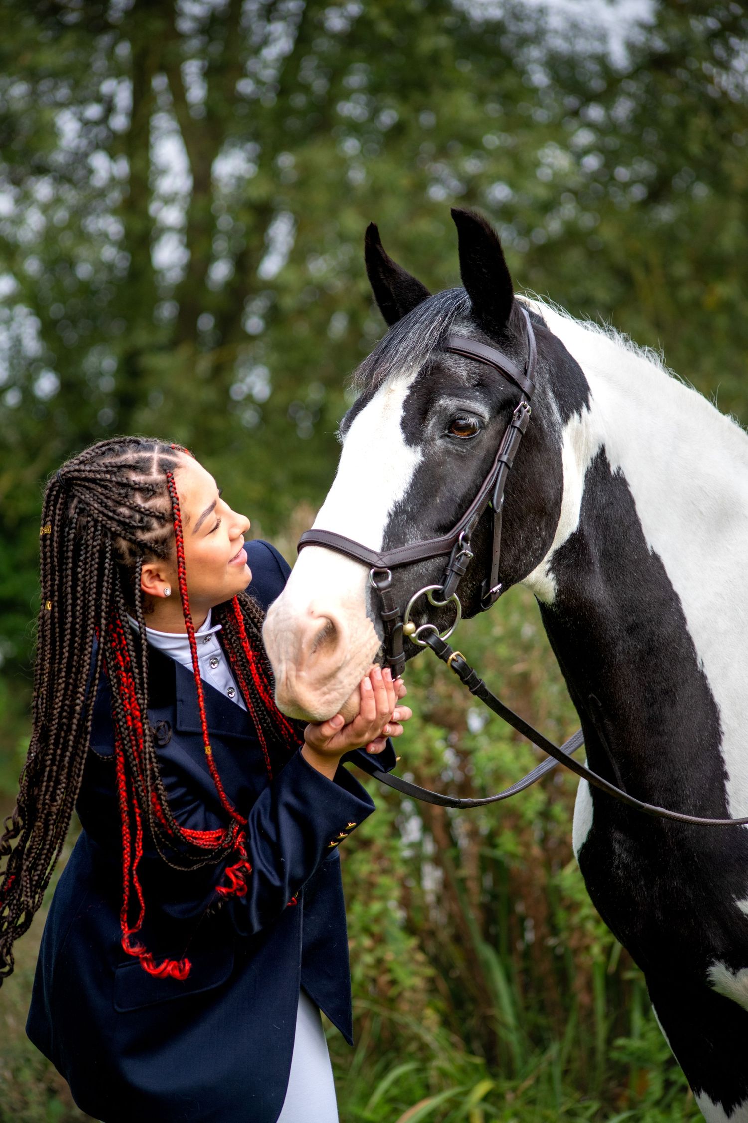Person with braided hair showing affection to black and white horse outdoors.