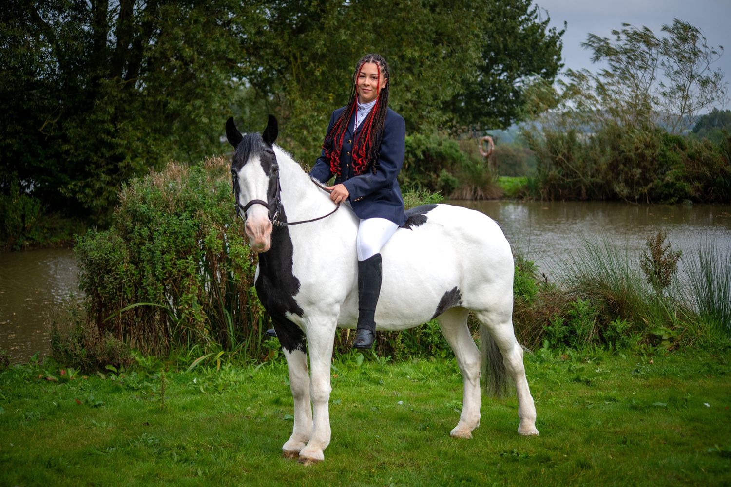 Equestrian posed on large black and white horse in countryside setting.
