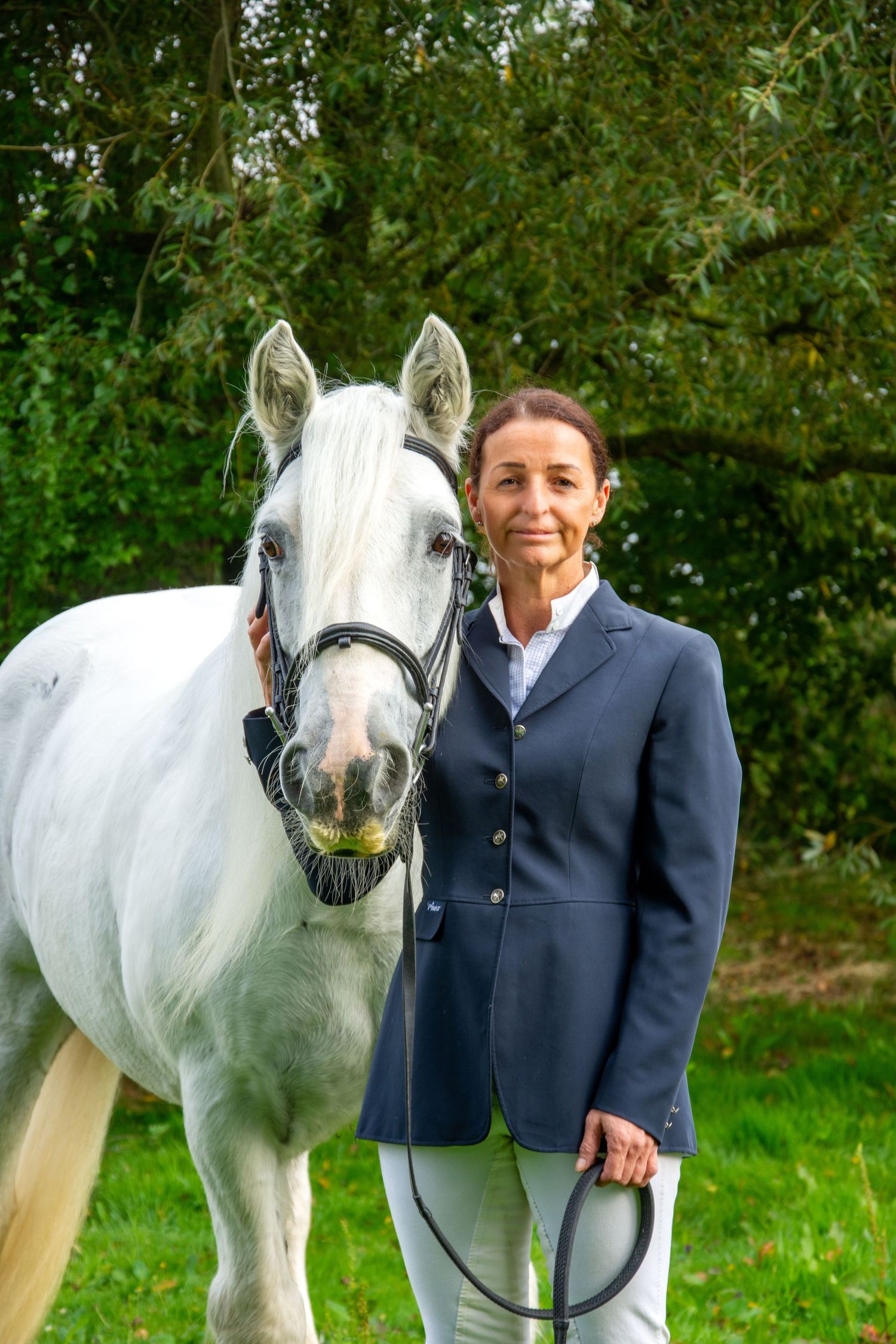 A handsome white horse poses with its handler in formal equestrian attire.