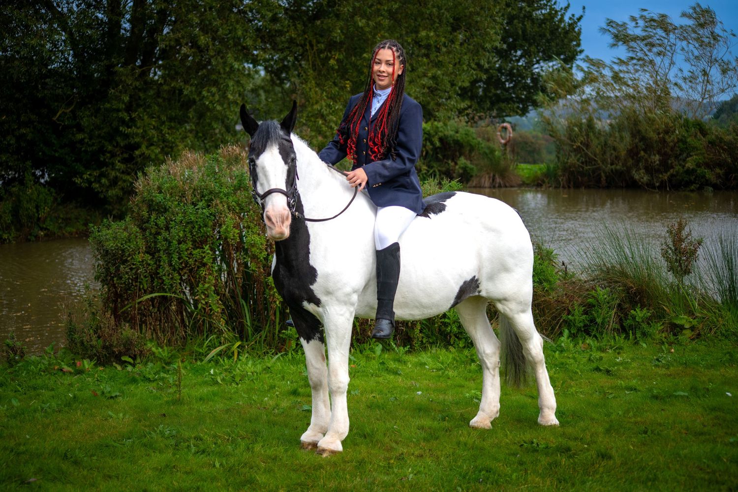 Rider in navy jacket mounted on white and black horse by riverside.