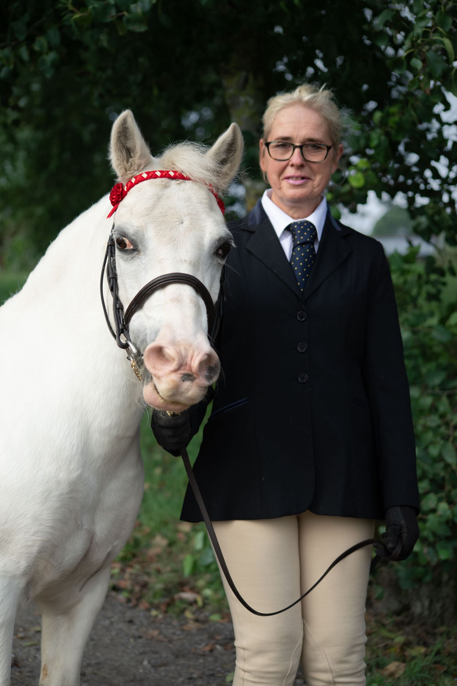 White horse wearing red browband with rider in formal equestrian show attire.