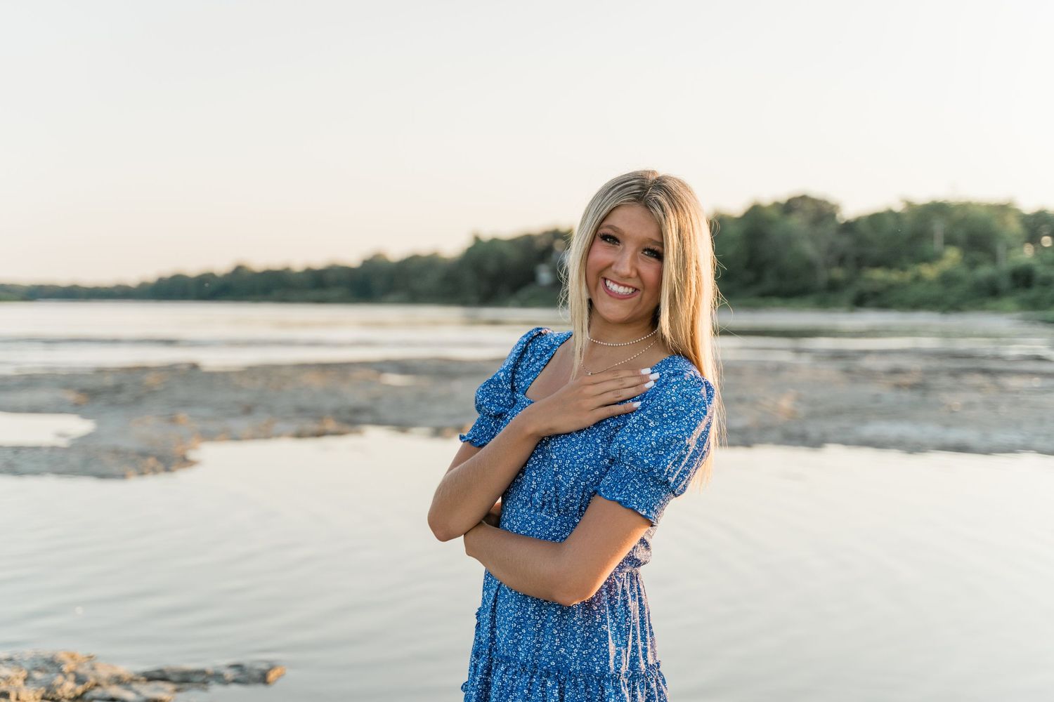 Senior in royal blue dress and sunhat posing along the Maumee River at Side Cut Metropark at golden hour.