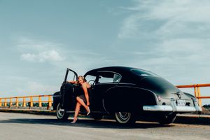 Retro-styled photo of a vintage black car on a bridge with door open.