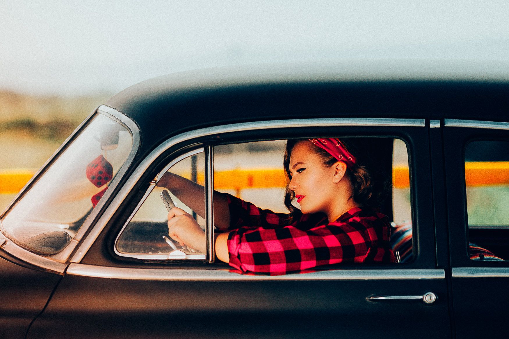 Classic black vintage car with someone wearing a red plaid shirt behind the wheel at sunset.