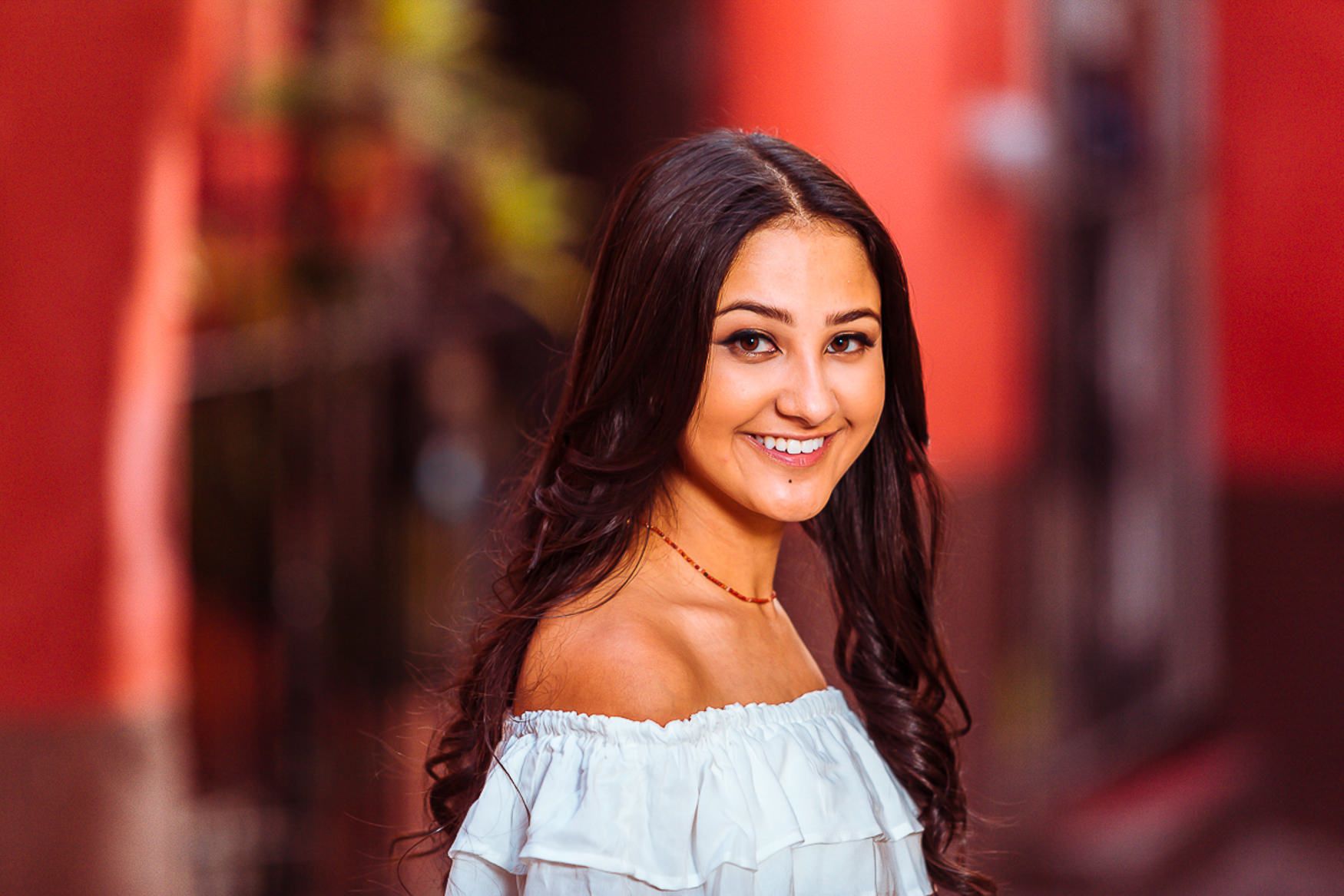An off-shoulder blue top contrasts with long dark hair against a red background.