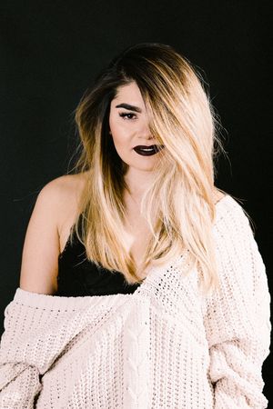 Fashion portrait against black background showing blonde hair and oversized knit sweater.