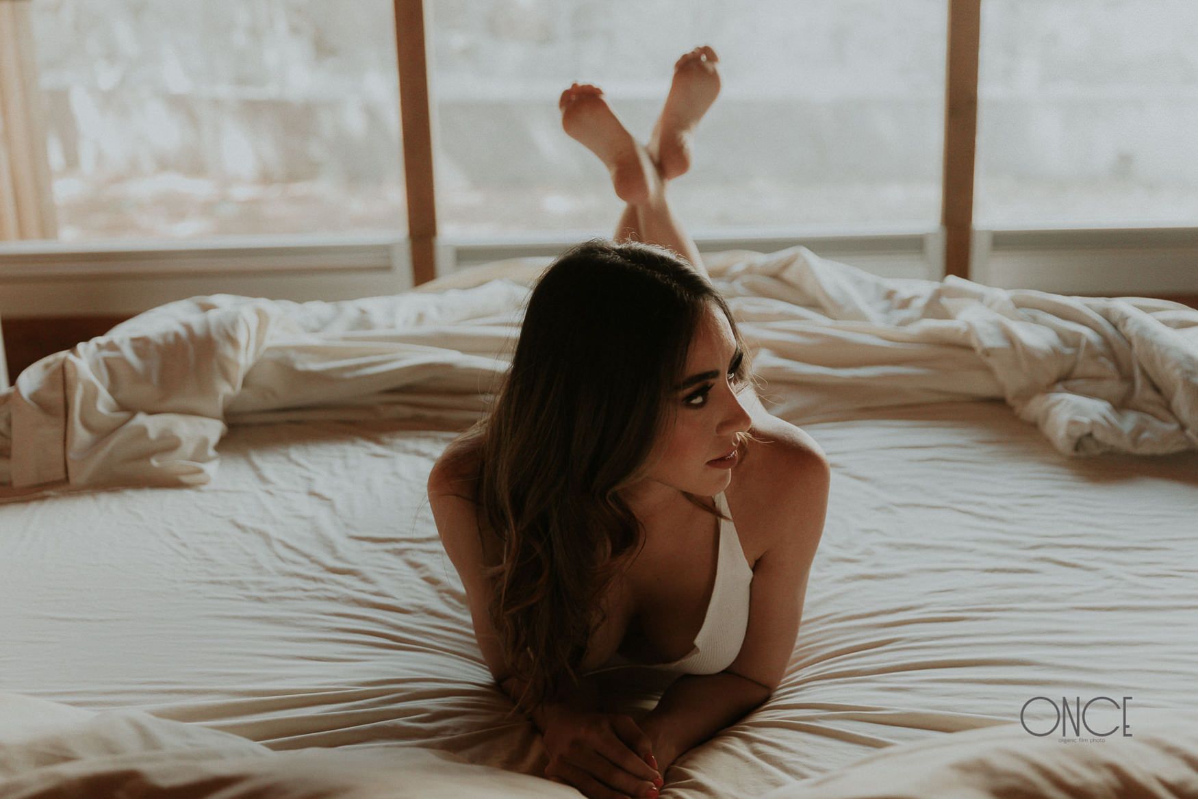 A relaxed figure lounges on white bedding in casual indoor attire.