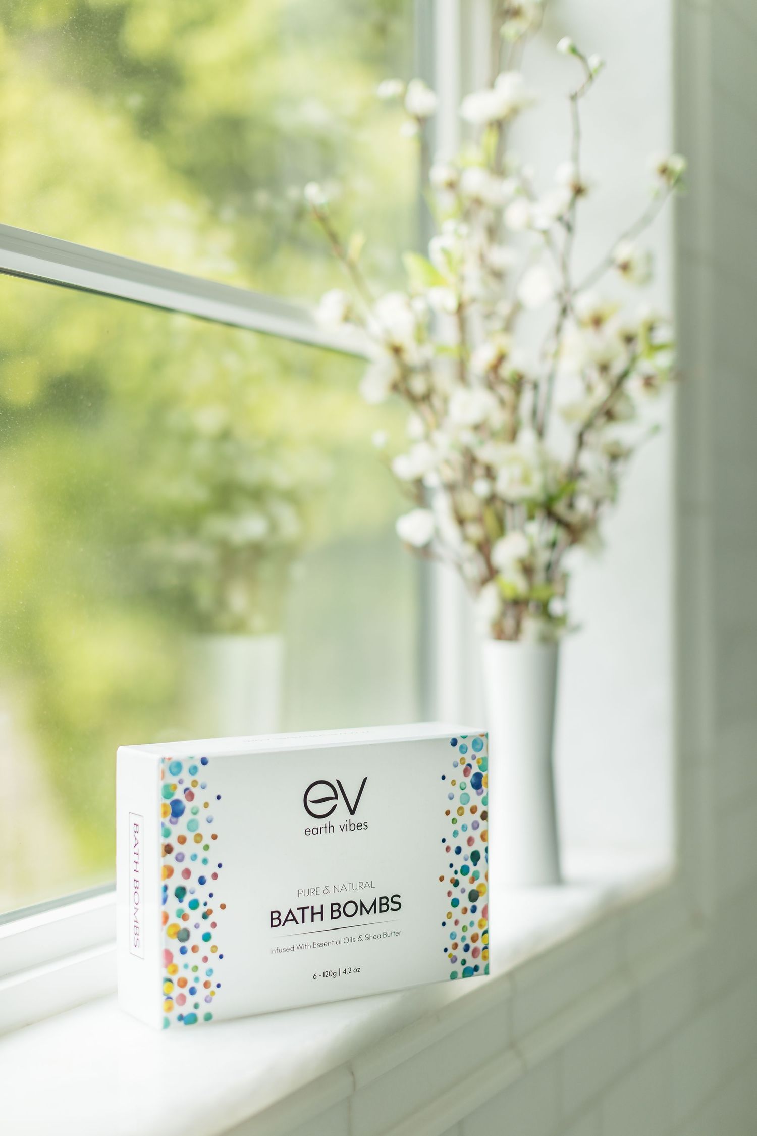 Bath bombs product packaging displayed on white windowsill with floral arrangement. Shot by Mika Larson Photography.