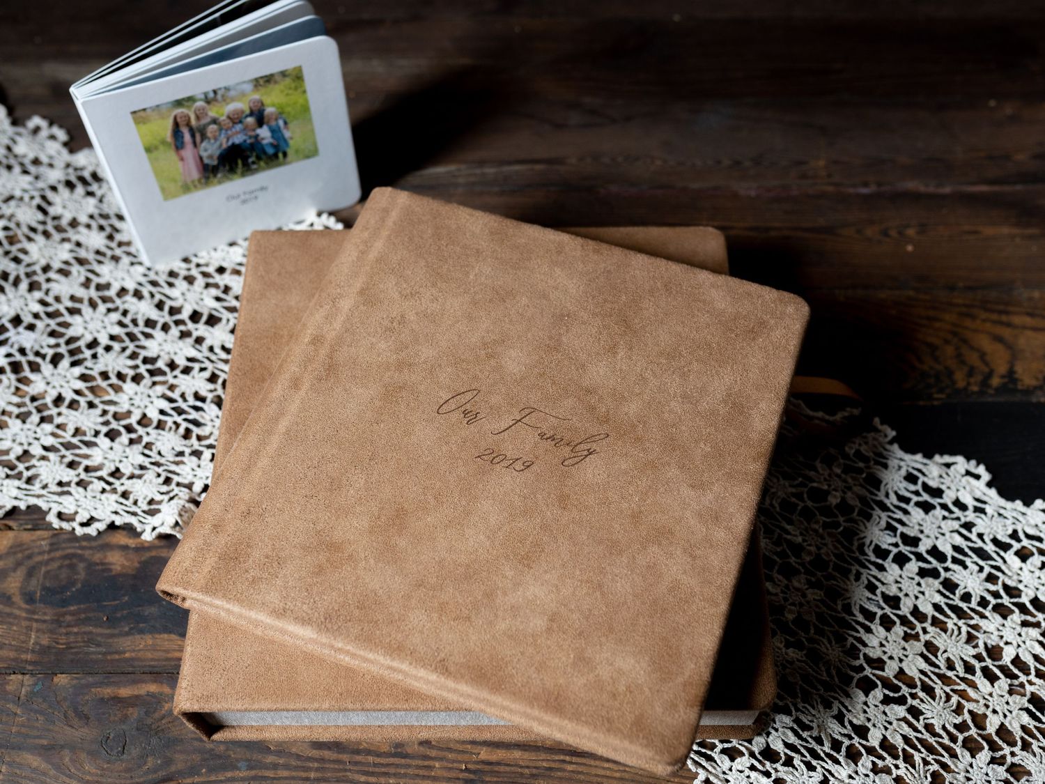 Leather photo albums and lace doily arranged on rustic wooden surface.