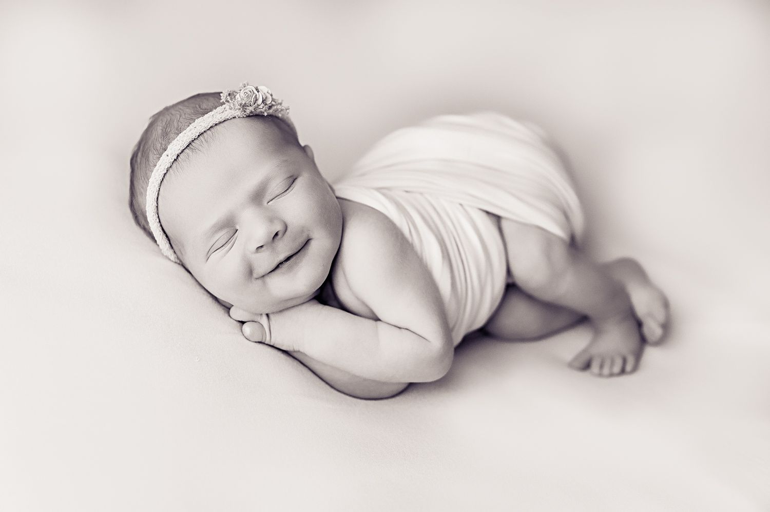 A sleeping newborn wrapped in white fabric wears a delicate crown in this black and white portrait.