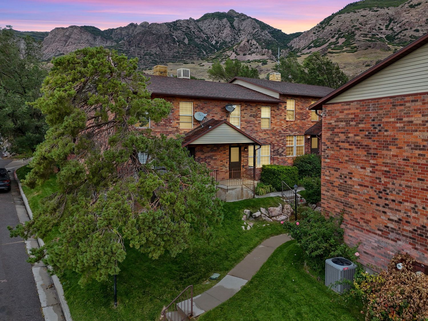 Brick townhomes with lush landscaping at dusk with mountain backdrop in Utah.
