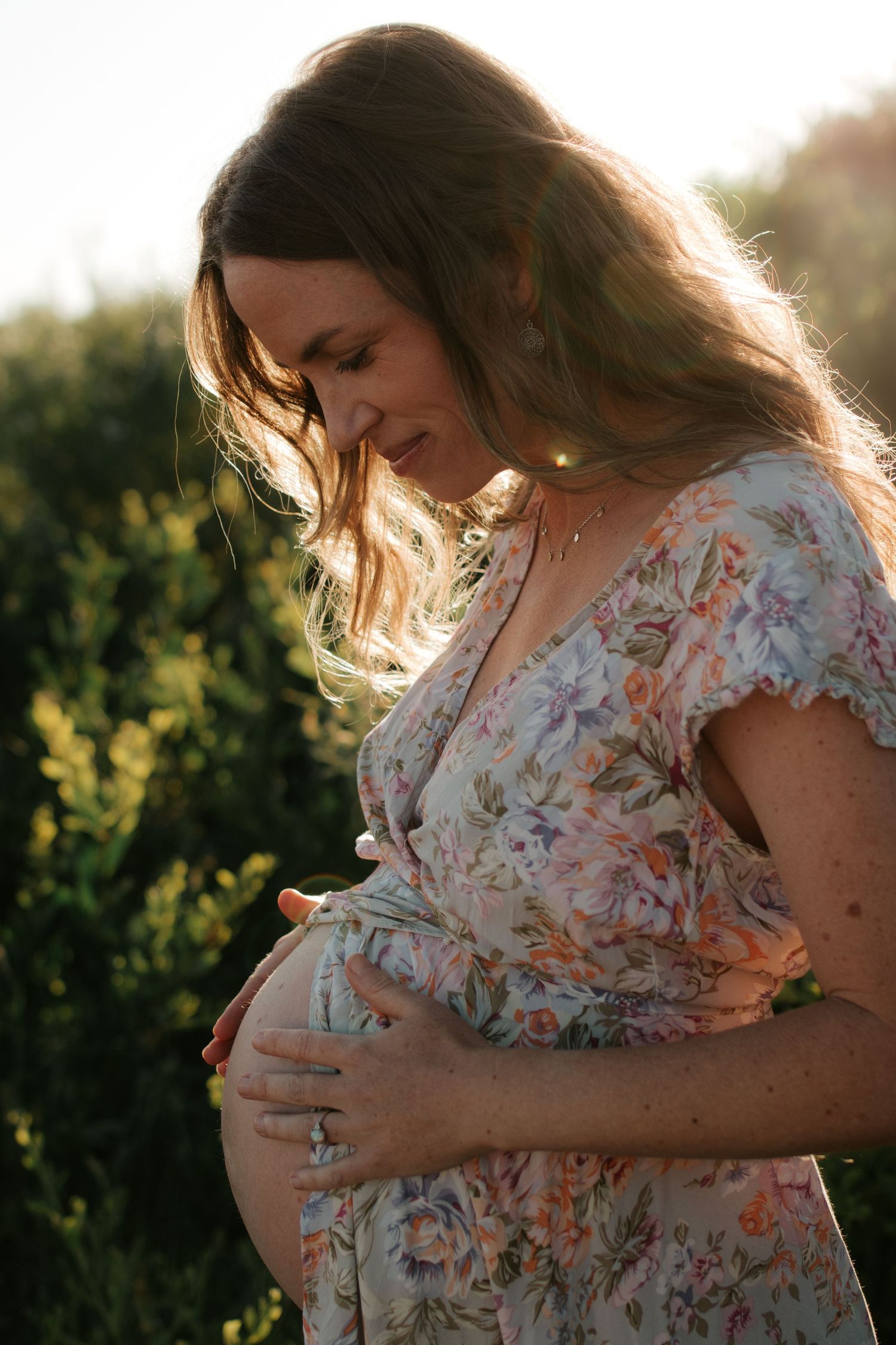 Tender maternity moment in a floral dress during golden hour.