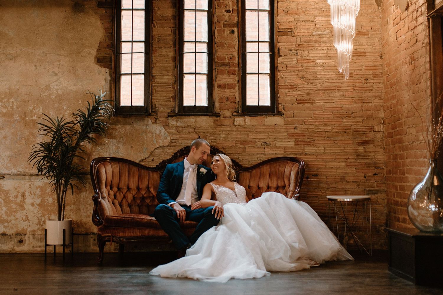 A romantic wedding portrait set in a rustic brick venue with vintage leather couch.