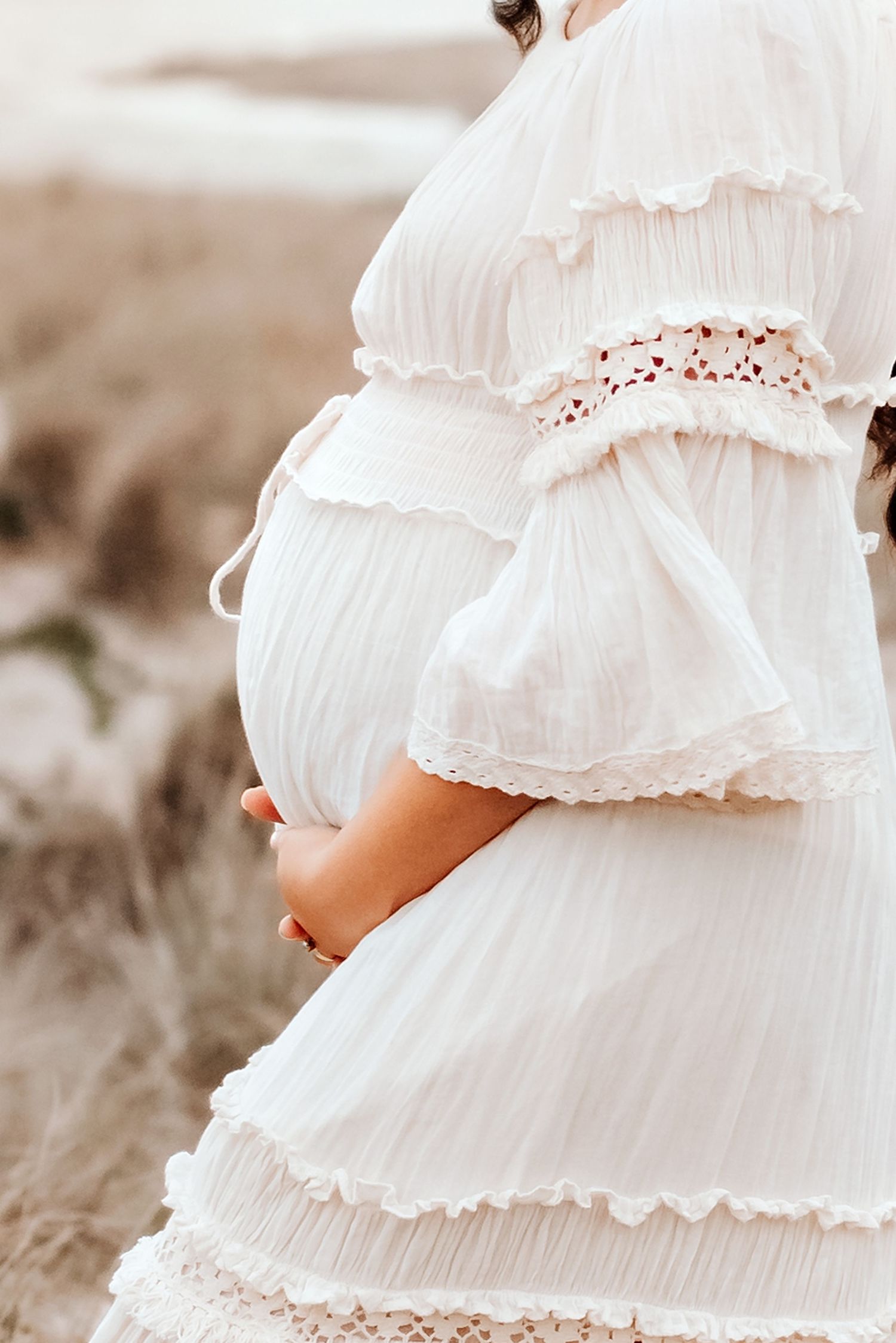Close up of a white ruffled maternity dress against a natural outdoor backdrop.