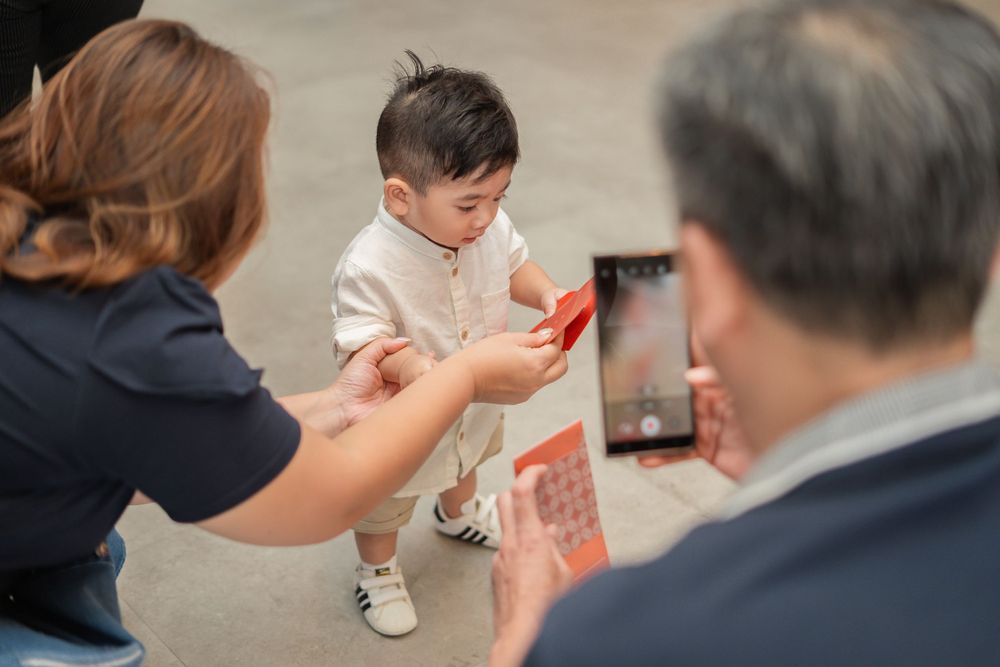 Adults interact with a small child holding a red object in an indoor setting.