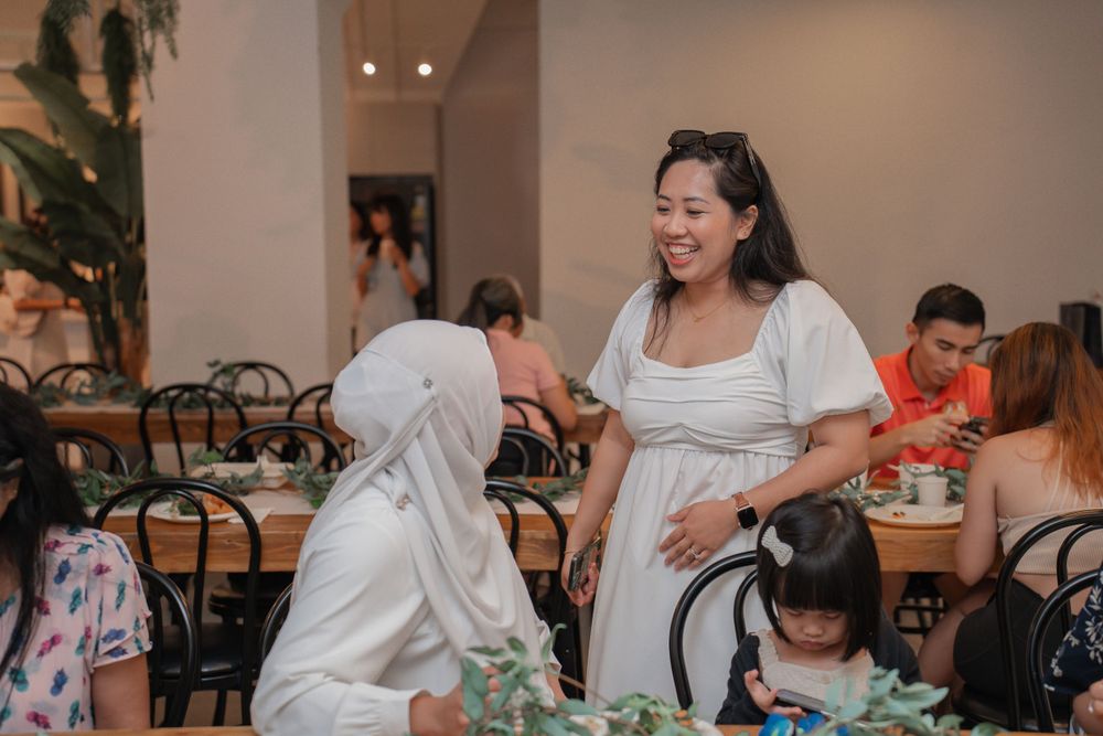 People gather for a meal at tables in a modern restaurant setting with greenery.