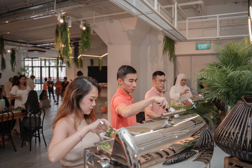 People gather around a food service station with decorative plants hanging from the ceiling.