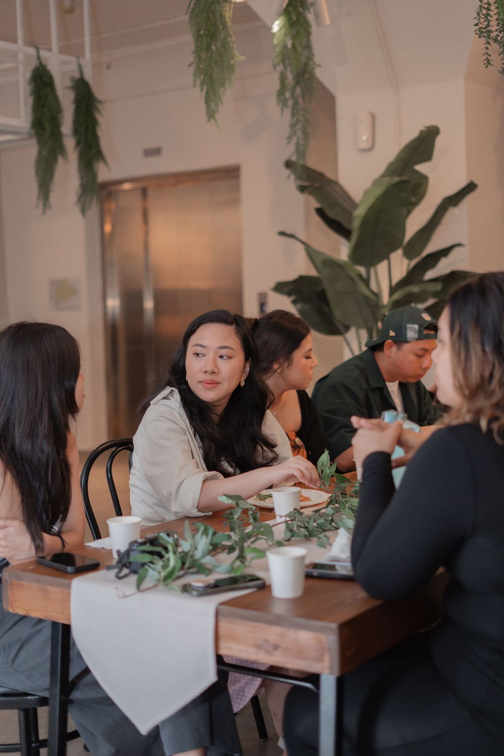 People gathered around a table for a social gathering with hanging plants decorating the space.