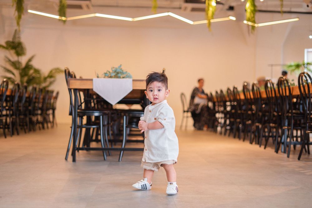 A small child in white clothing walking across an empty event venue with chairs in the background.