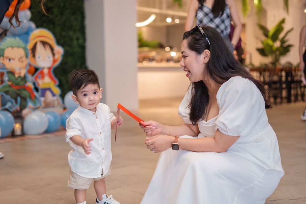 People interact with a toddler in a decorated indoor space with cartoon characters on the wall.