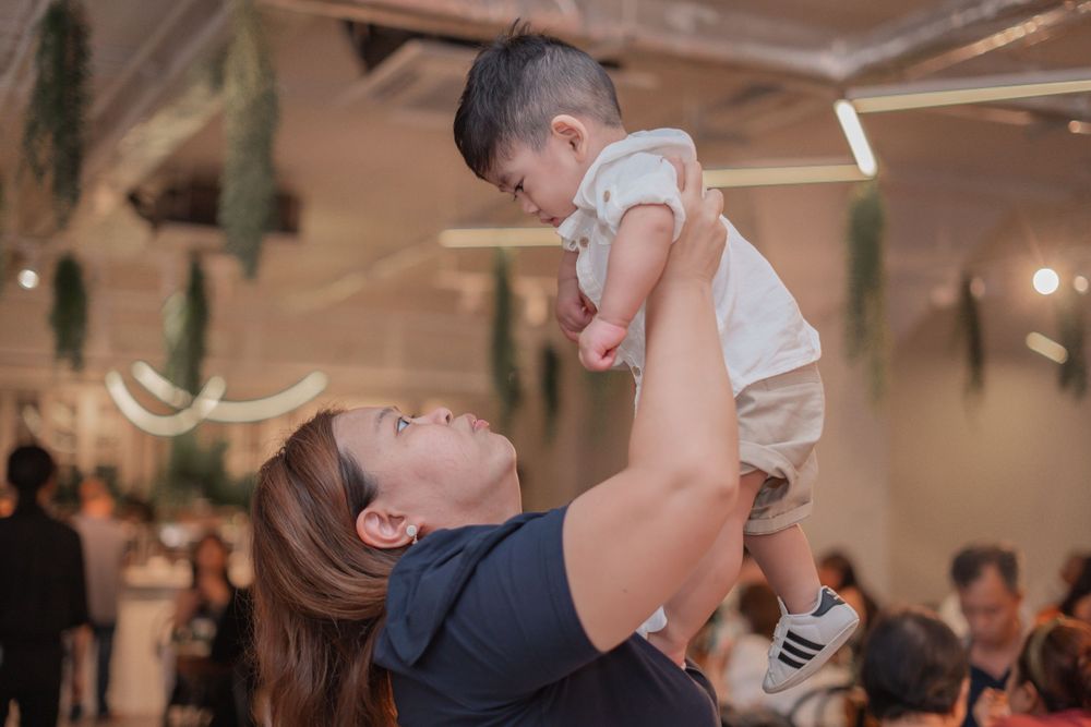 A joyful moment at an indoor celebration as a baby is lifted high in the air.