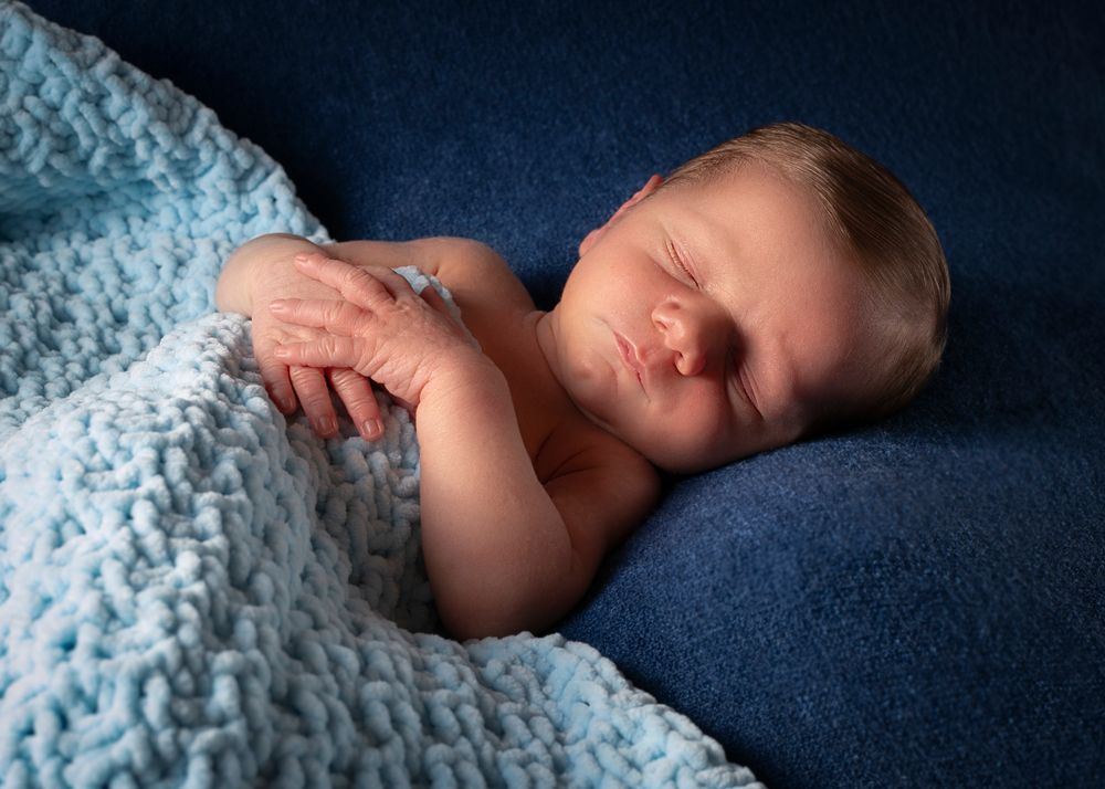 New born baby boy asleep on dark blue background covered with a blue blanket