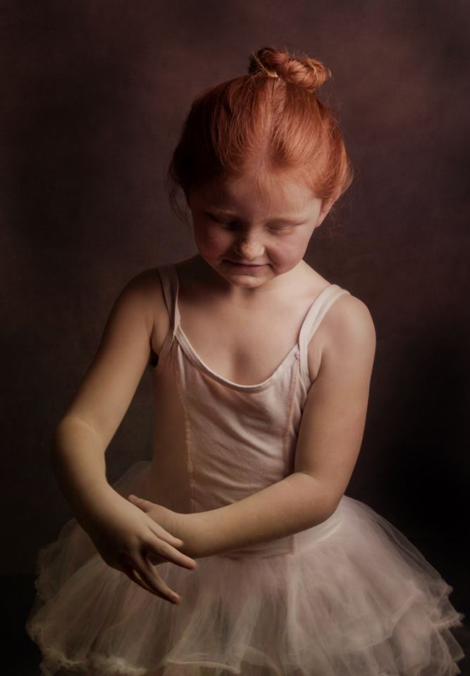 fine art portrait photo of young girl looking down in ballet tutu with hair in bun