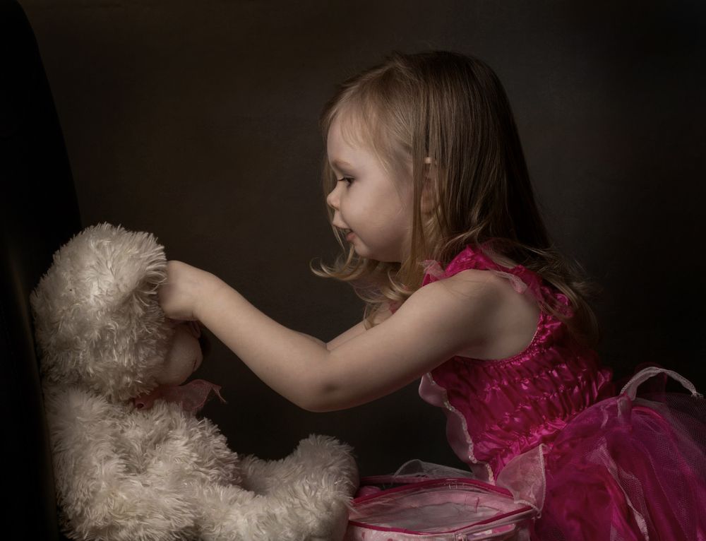side view portrait of little girl in pink dress playing with a teddy bear